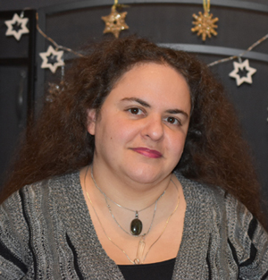 white woman with brown frizzy wavy hair, behind her a couple stars from a hanging garland