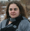 white woman with brown hair, outside in gray and black sweater and scarf, looking to the side pondering