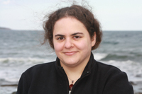 white woman with brown hair worn up, behind me is water with small waves coming in